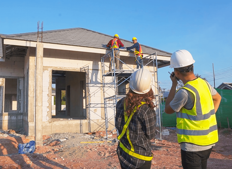 Asian male construction engineer talking to Asian female architects. standing at a construction site to explain install solar cells on the roof of the house.